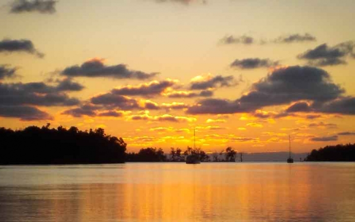 a sailboat floats in the distance in calm water at sunset